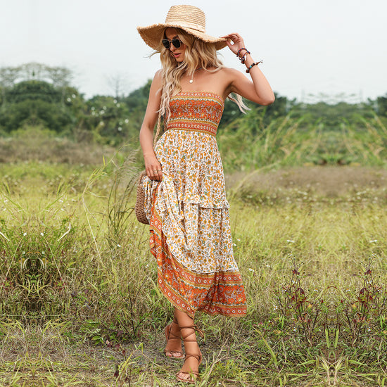 Woman in a patterned dress and straw hat standing in a grassy field.